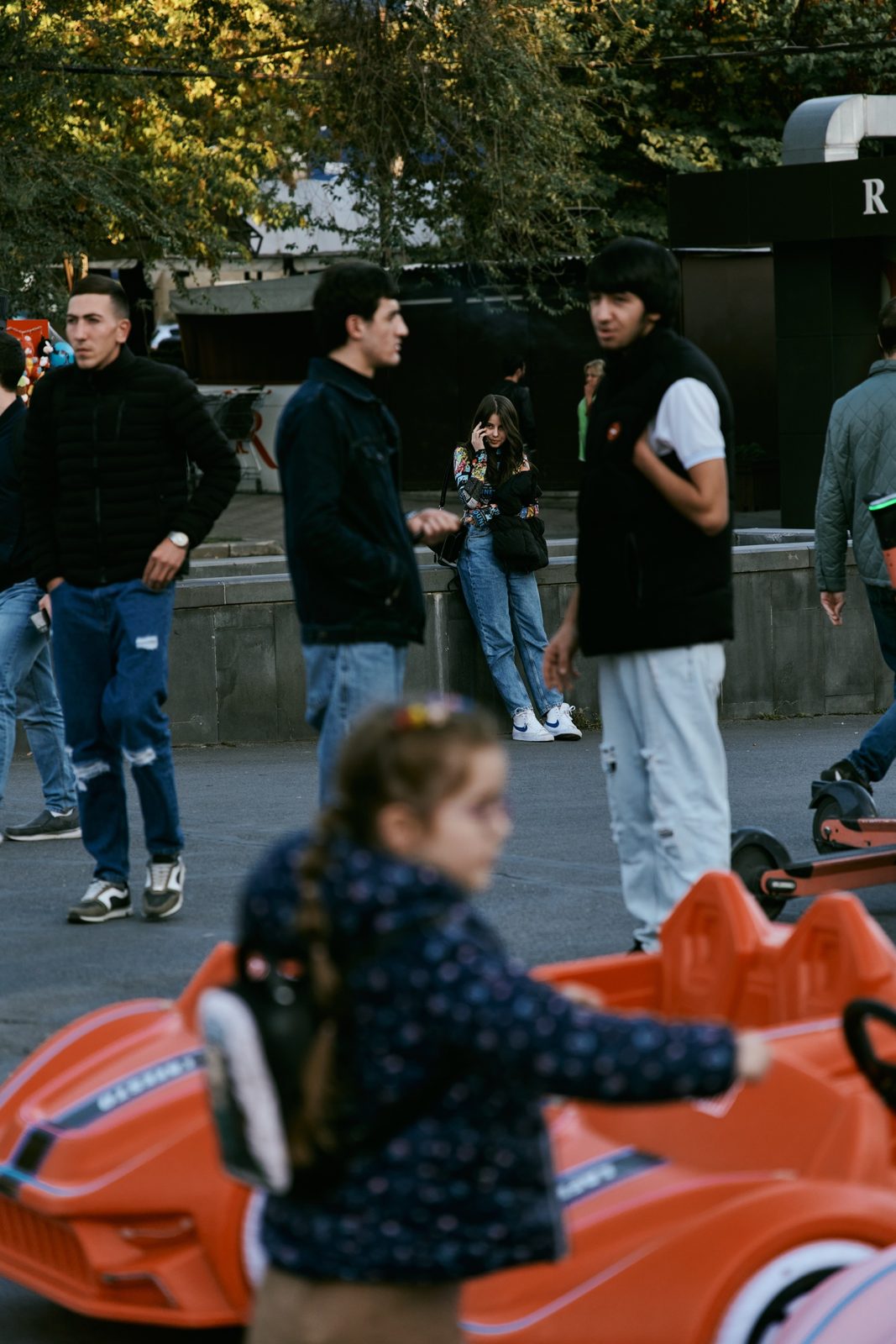 A girl in a toy car among young men on a city square, Yerevan, Armenia