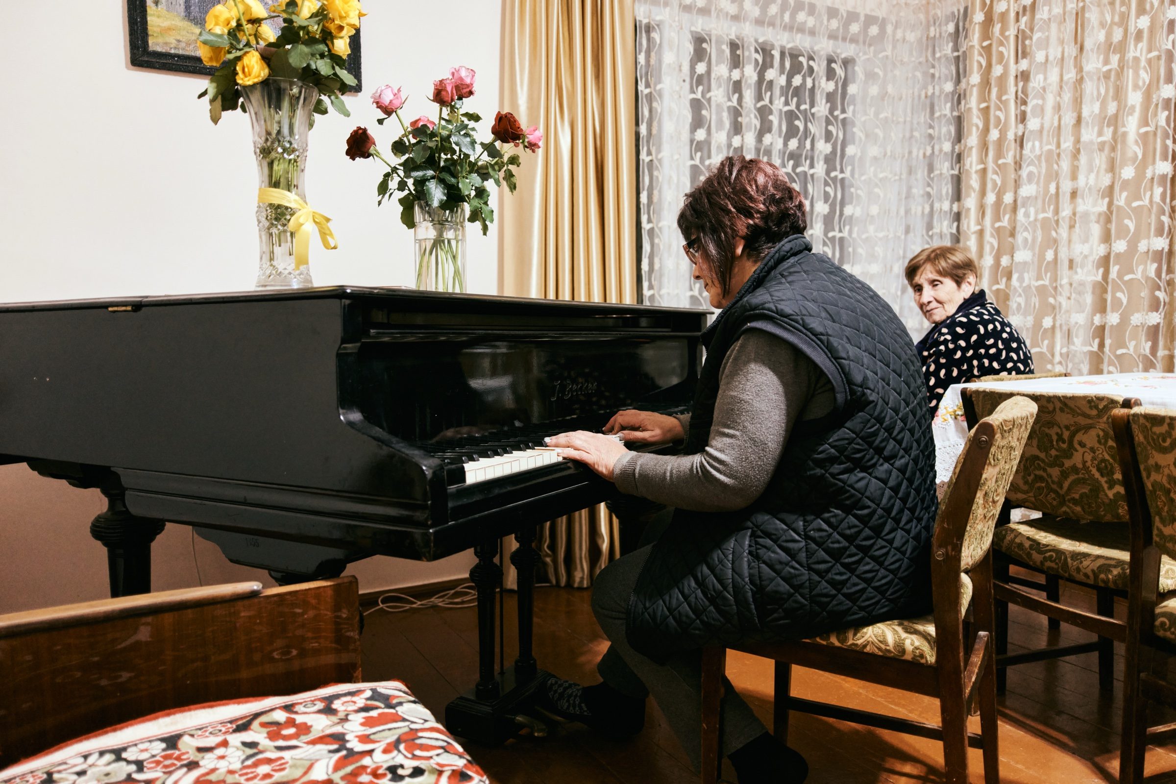 A woman playing a grand piano in a home dining room as another woman looks on, Armenia