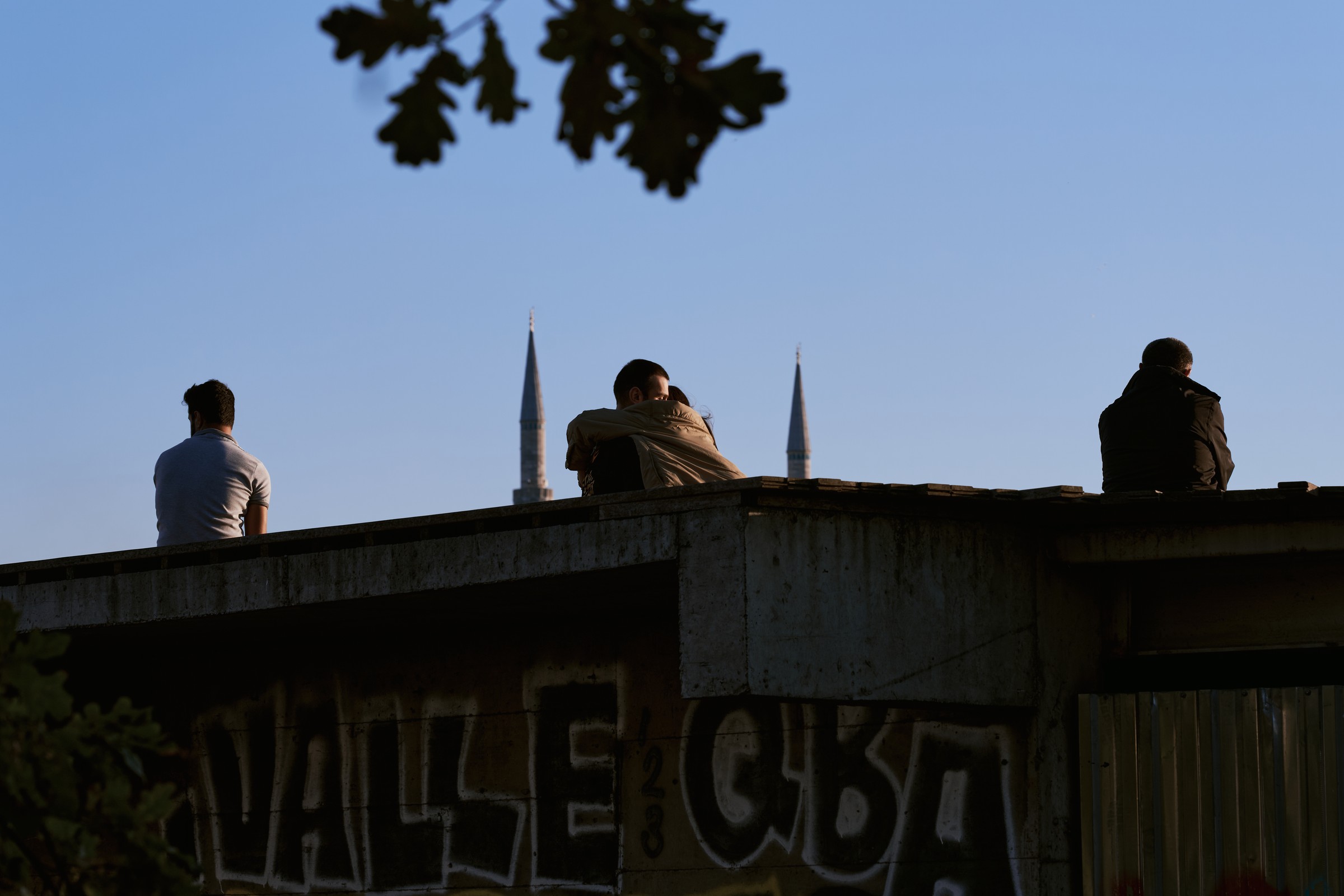 People sitting on a graffiti-covered rooftop between two minaret silhouettes, Istanbul