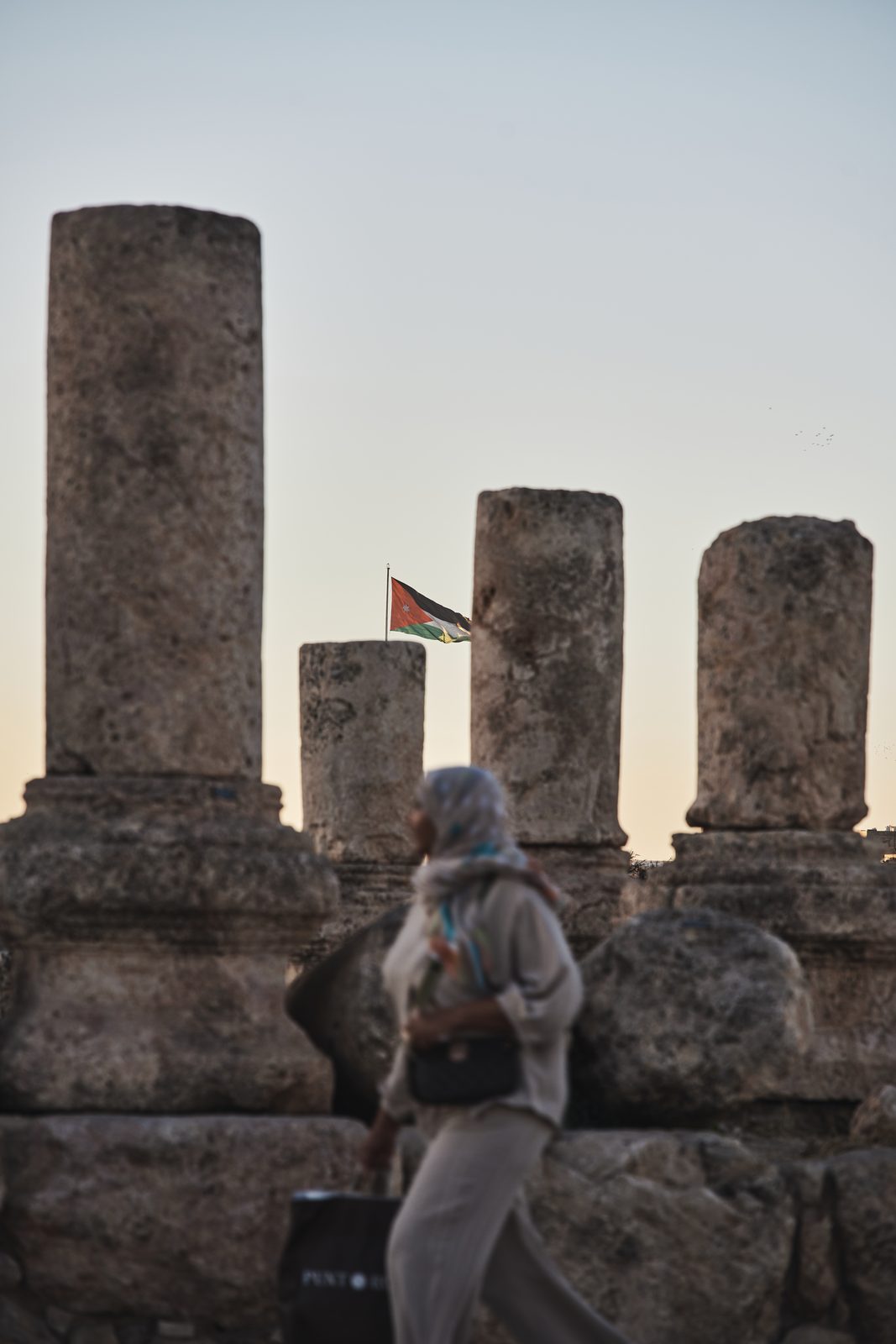 Ancient columns with a flag and a passing woman