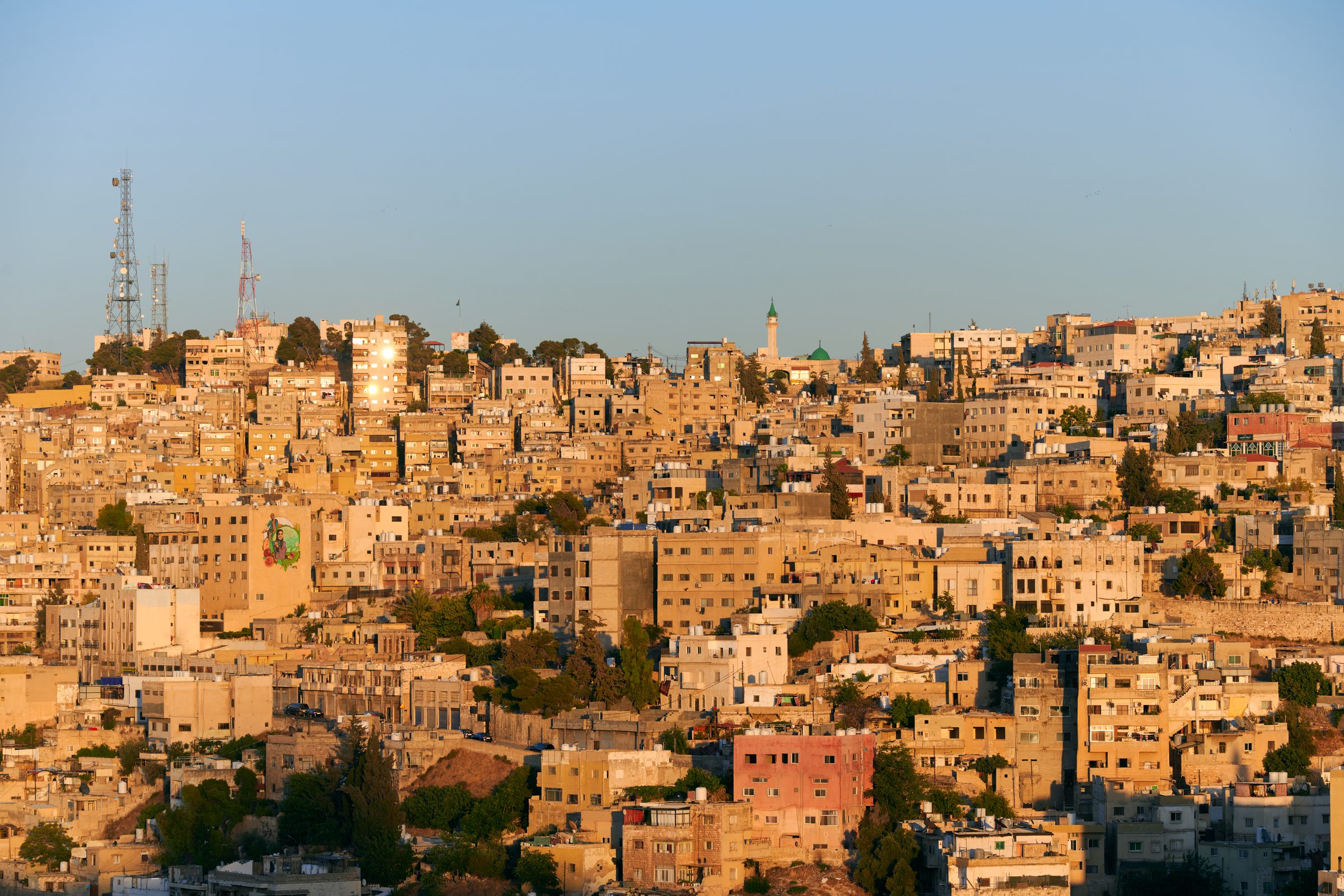 Sunlit hillside of houses with a green minaret under blue sky