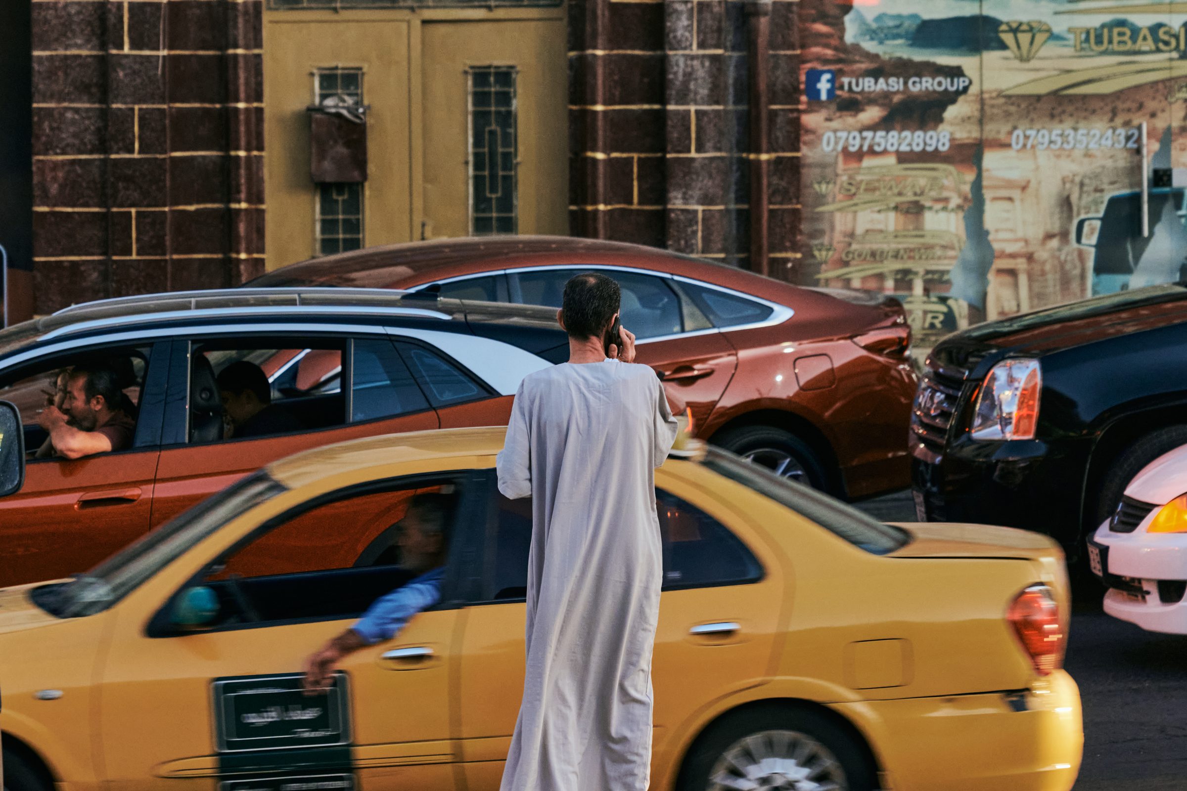 Man in a robe beside a yellow taxi, traffic blurred