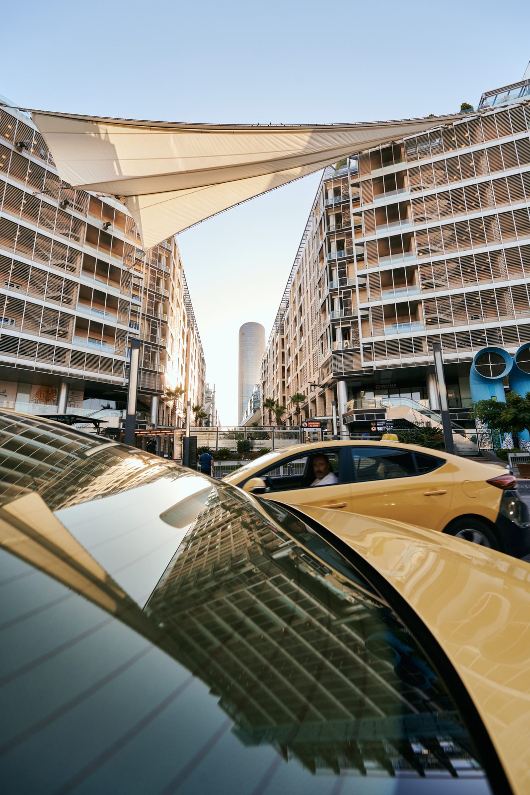 Towers and a sail shade reflected in a car roof