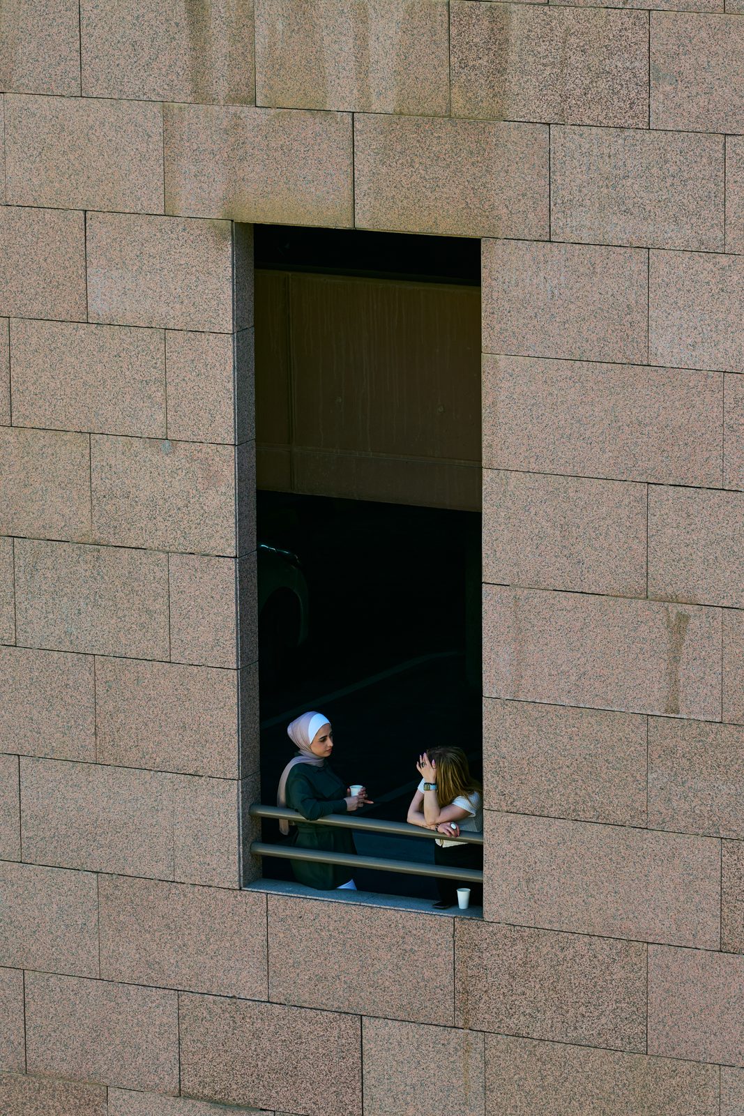 Two figures in a window of a stone wall