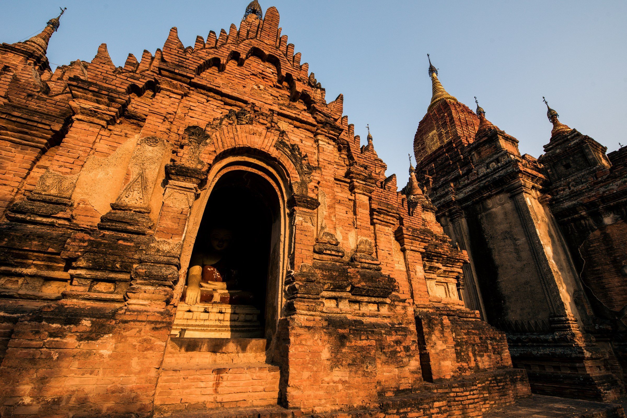 Brick temple facade with a seated Buddha in a shadowed alcove, Bagan, Myanmar