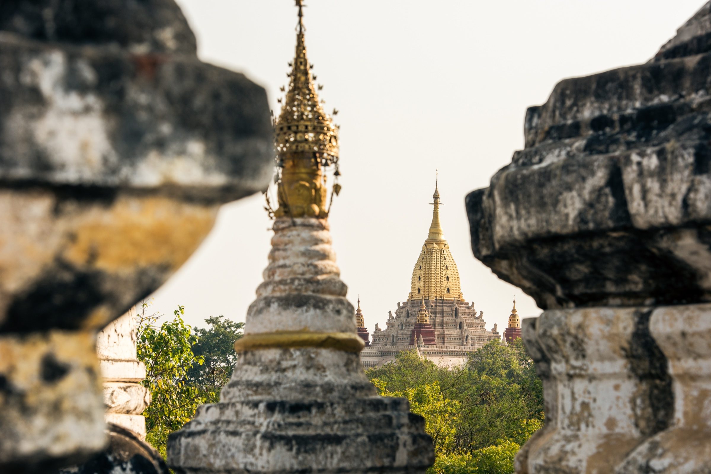 A golden pagoda spire framed between weathered stupa tops, Bagan, Myanmar