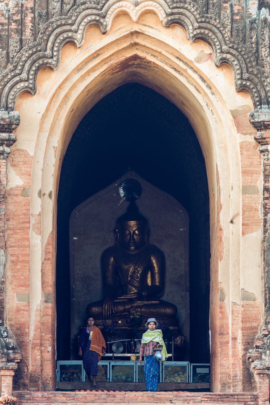 Visitors beneath a seated Buddha statue in a temple archway, Bagan, Myanmar