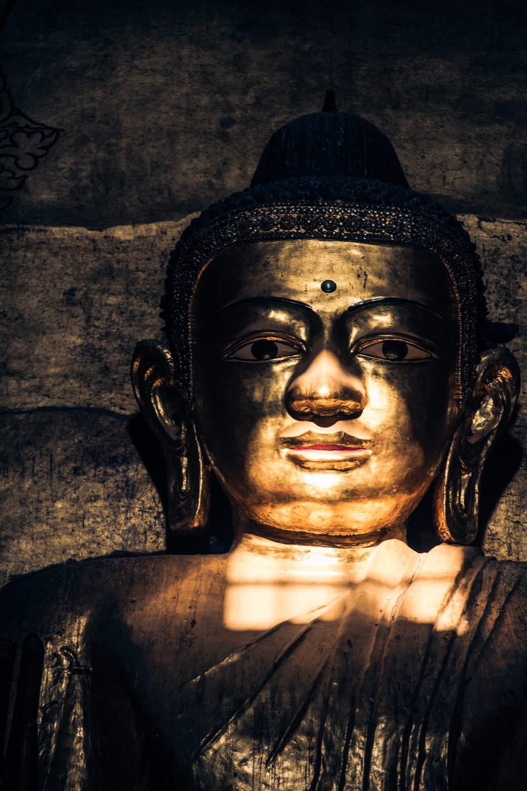 Close-up of a golden Buddha face in dramatic light, Myanmar