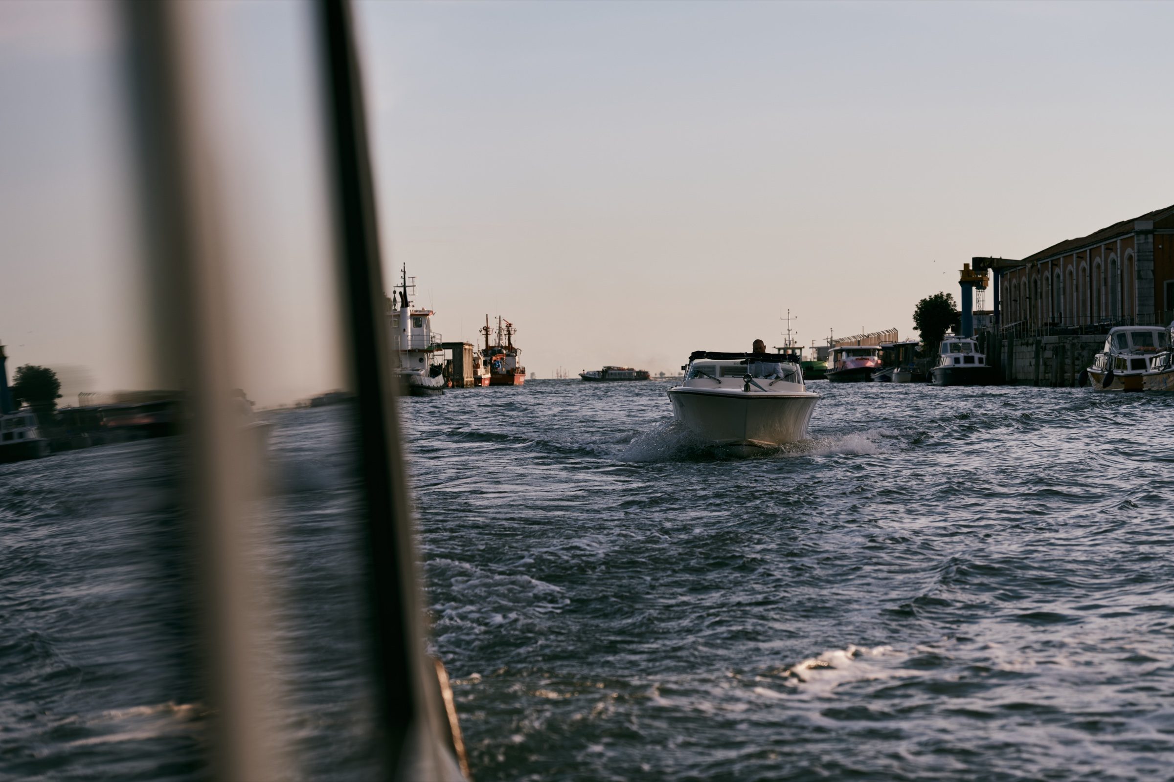 A motorboat cutting through the lagoon, seen past the edge of a vaporetto window, Venice