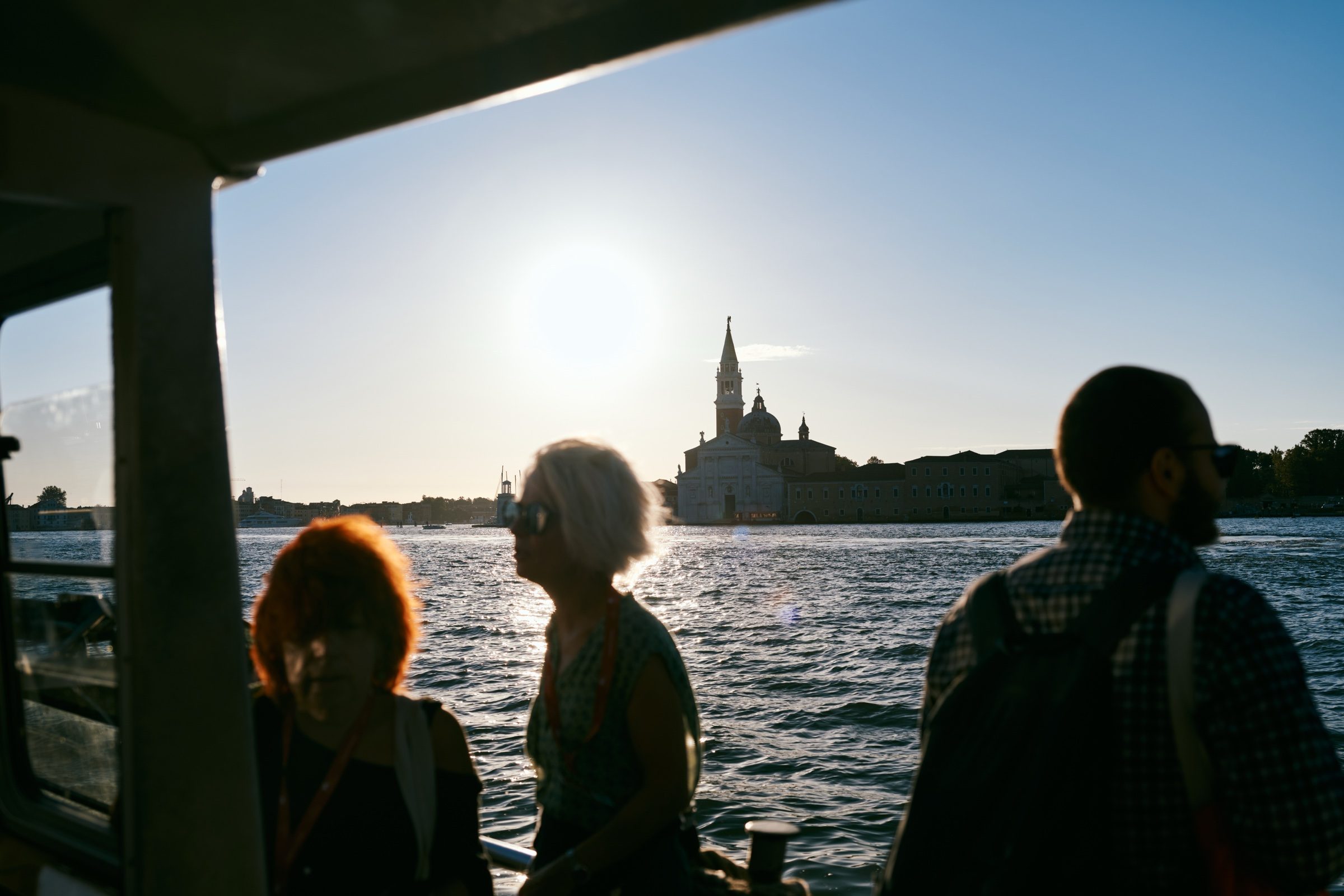 Passengers silhouetted against the setting sun on a water bus, San Giorgio Maggiore in the distance, Venice