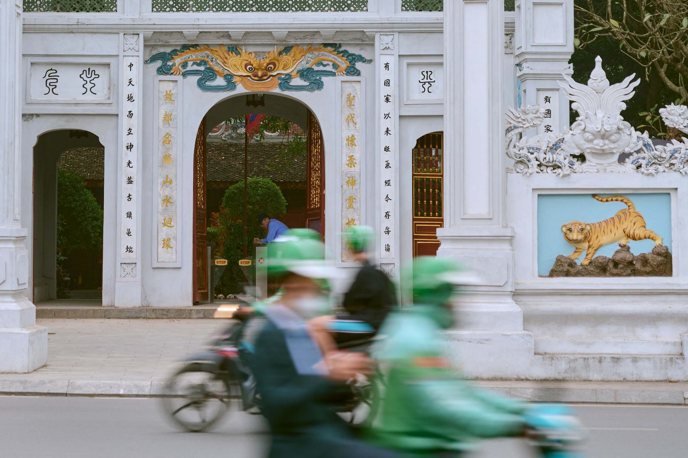 Dragon-crowned gate of Ngoc Son Temple with a tiger relief and motorbikes blurring past, Hanoi, Vietnam