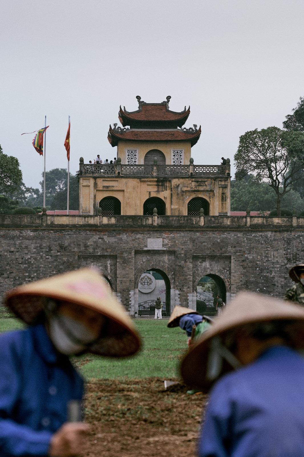 Imperial Citadel of Thang Long gate behind blurred conical-hatted workers, Hanoi, Vietnam