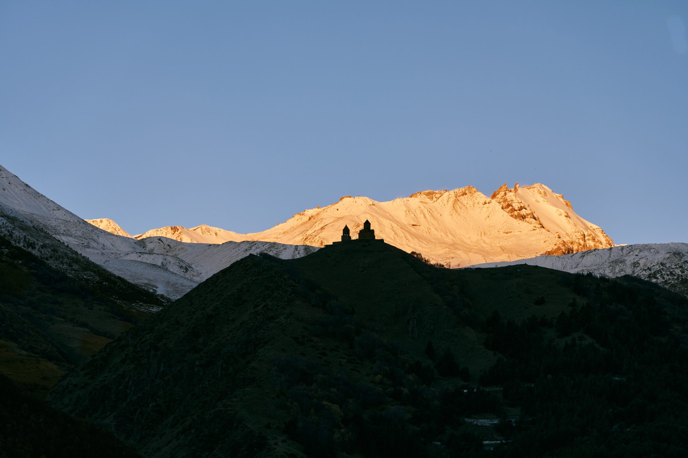First light on the Kazbek massif, with Gergeti Trinity Church silhouetted on the dark ridge below, Georgia