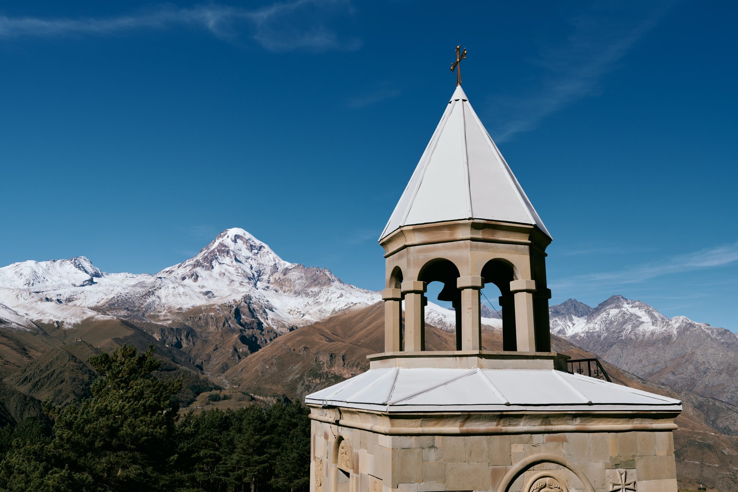 Stone bell tower of Gergeti Trinity Church in front of snow-capped Mount Kazbek, Georgia