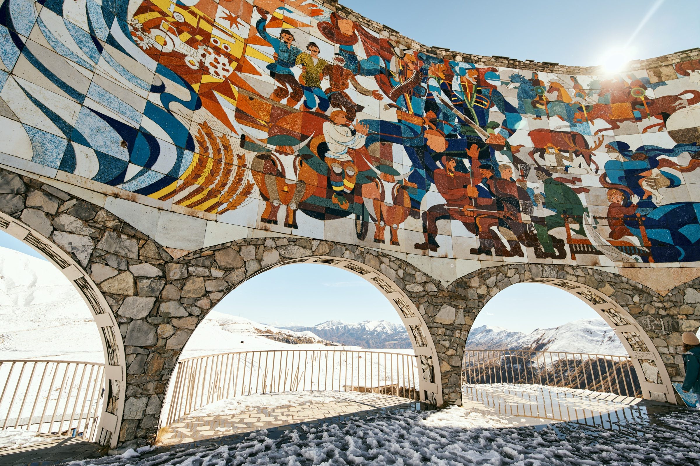 Sun flaring over the colourful Soviet-era mosaic and stone arches of the Russia–Georgia Friendship Monument, Georgia
