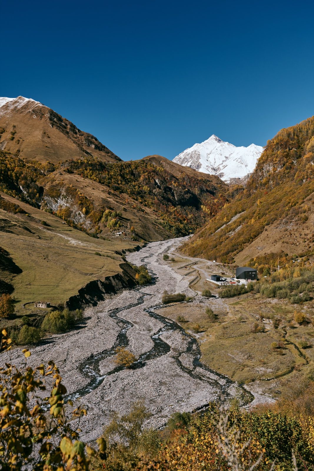 A braided river winding through an autumn valley toward a snowy peak, Georgia