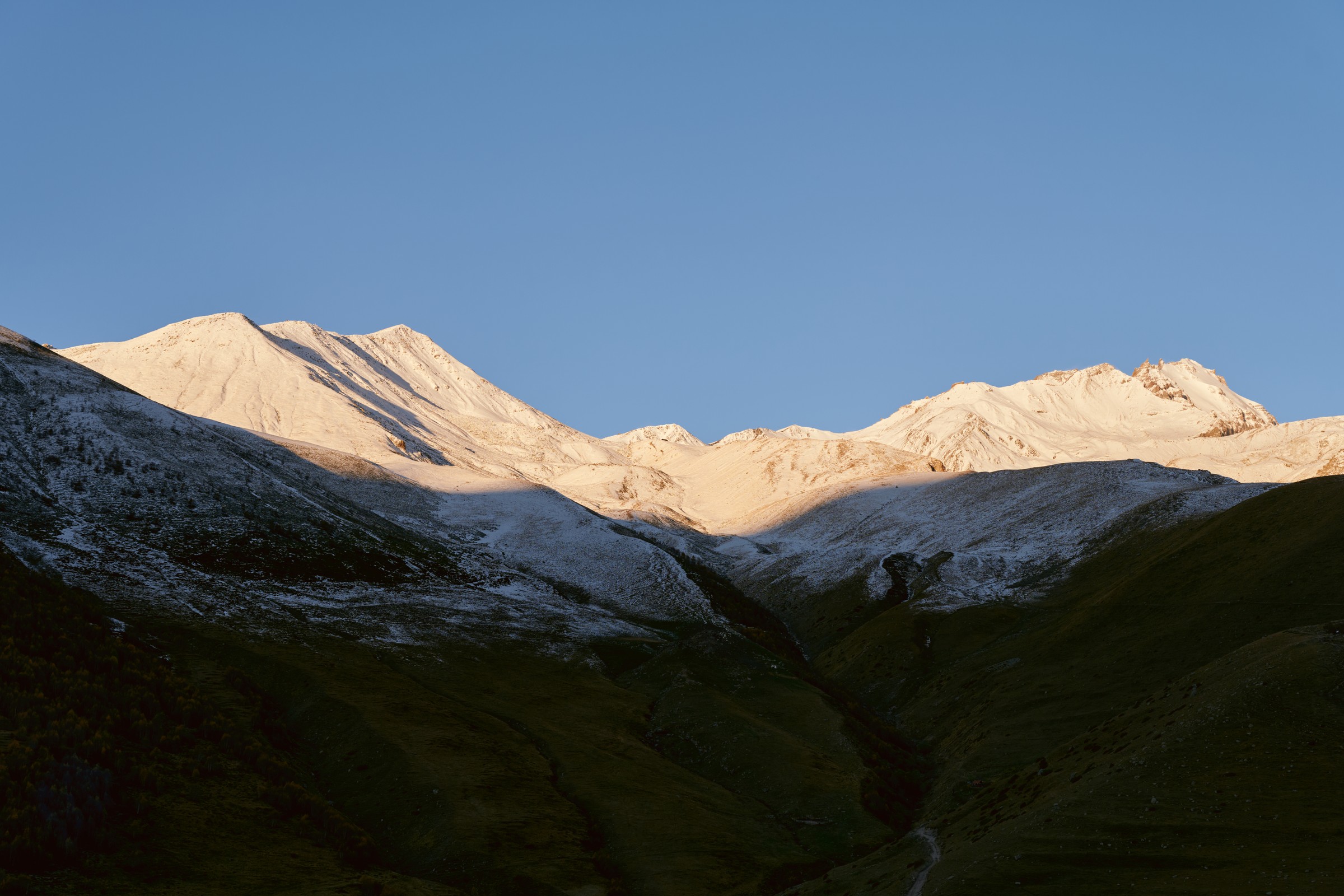 Sunrise light turning the Kazbek snow ridges gold while the valley stays in shadow, Georgia