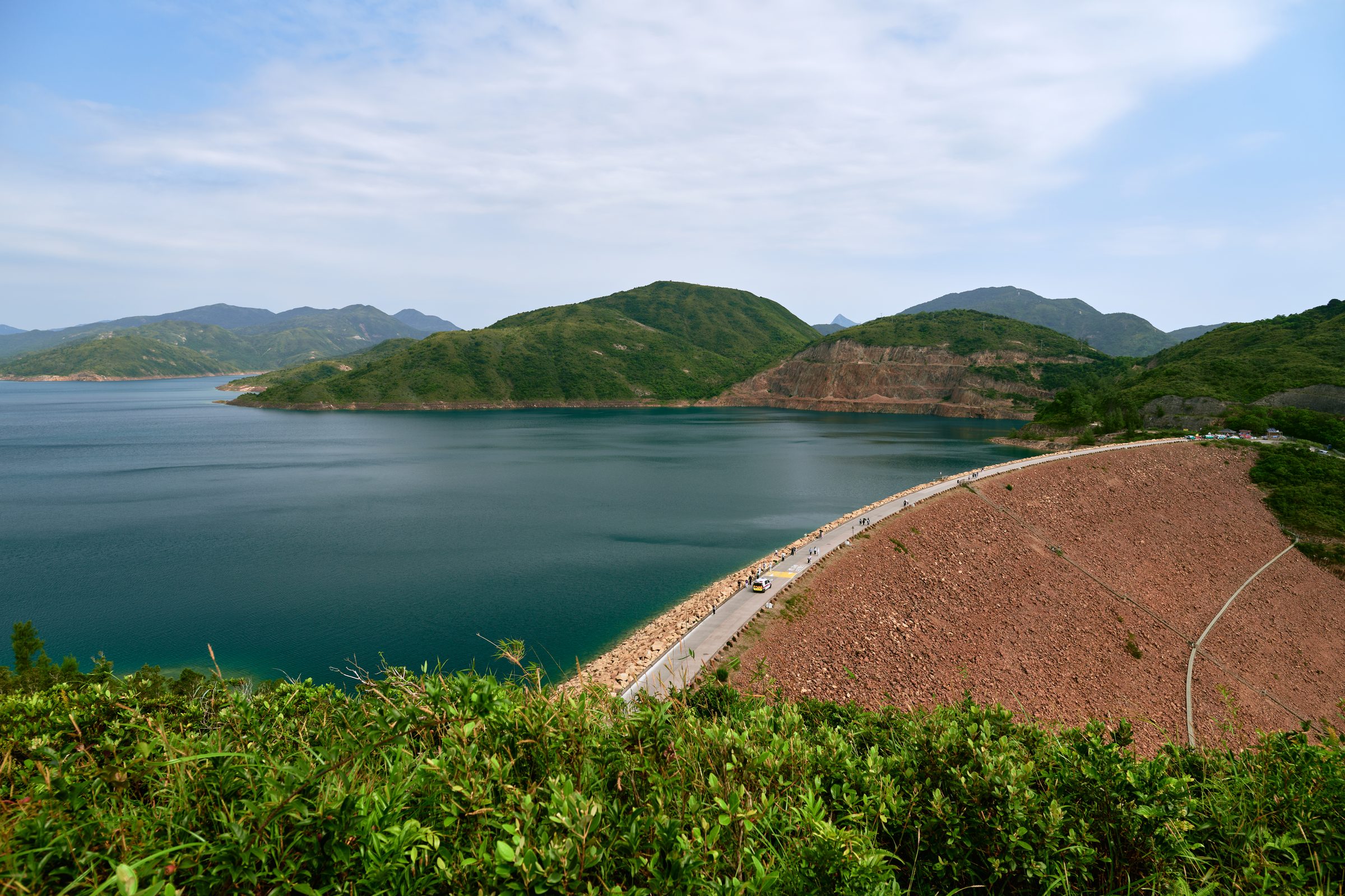 Reservoir dam road curving beside the water, seen from the MacLehose Trail, Sai Kung, Hong Kong