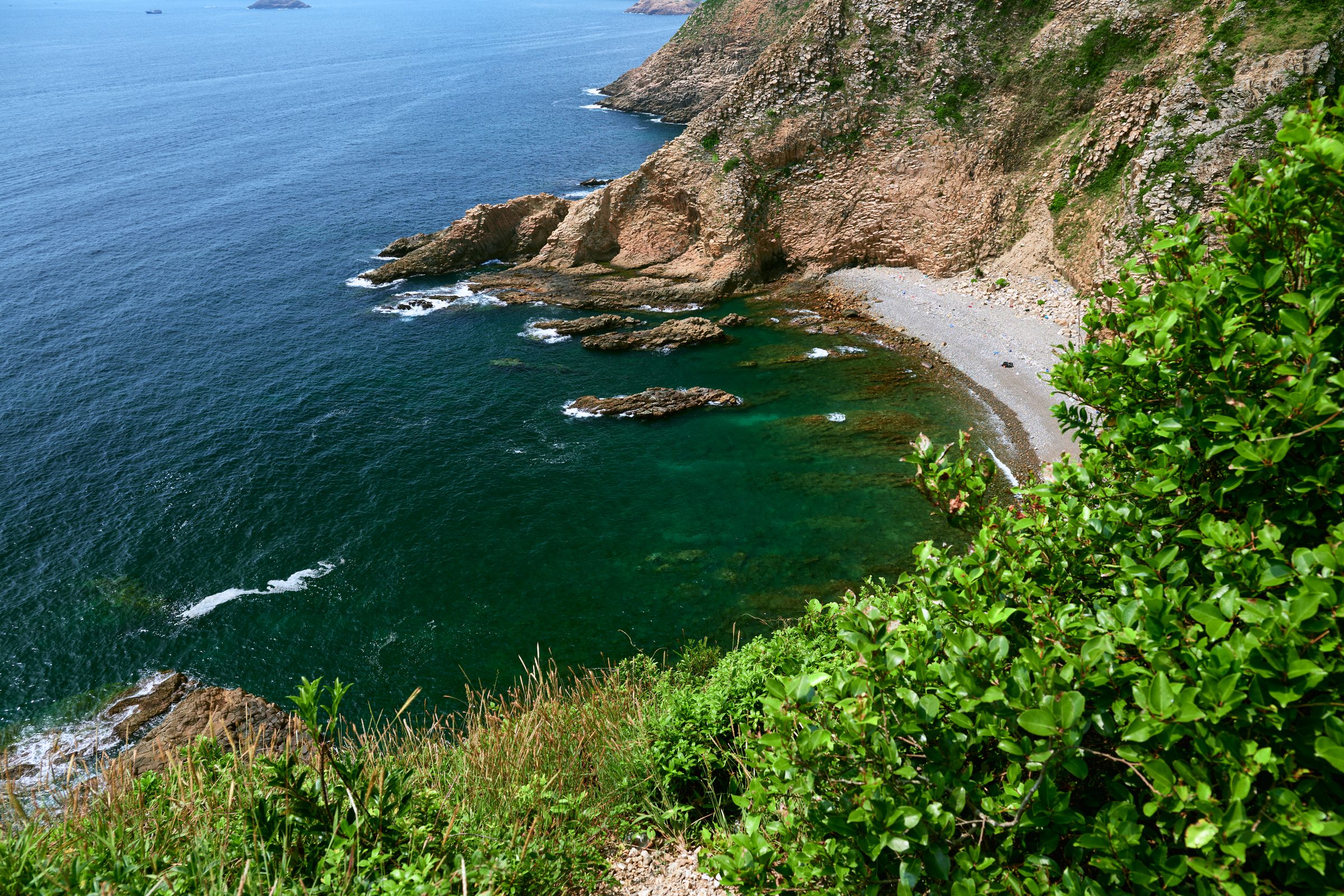 Rocky cove with a pebble beach and deep blue water seen from above, MacLehose Trail, Sai Kung, Hong Kong