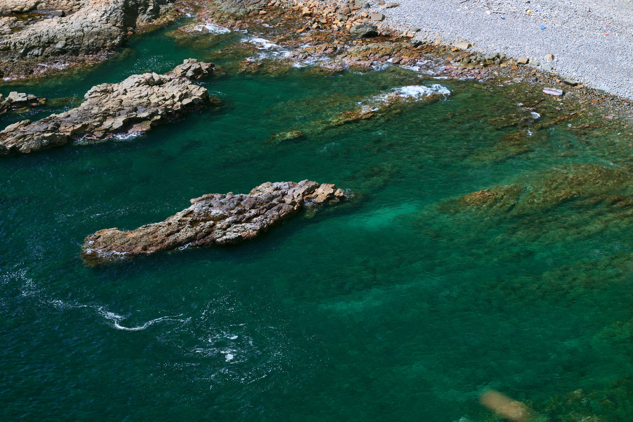 Turquoise water around rock outcrops and a pebble beach from above, MacLehose Trail, Sai Kung, Hong Kong