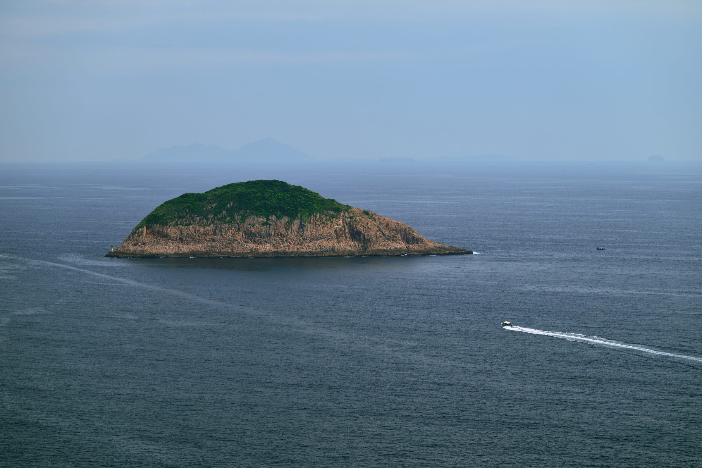 Small green island in open sea with a speedboat wake, seen from the MacLehose Trail, Sai Kung, Hong Kong