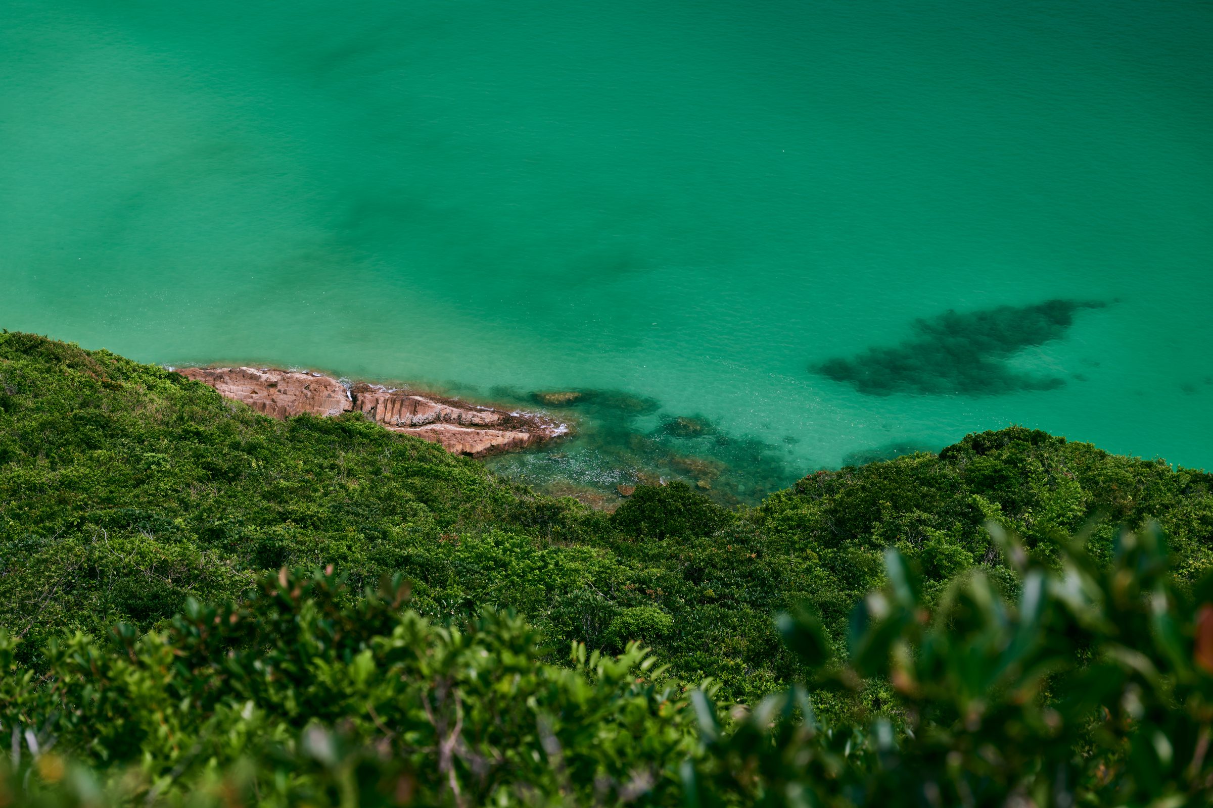 Emerald water and a rocky shoreline below green hillsides, MacLehose Trail, Sai Kung, Hong Kong