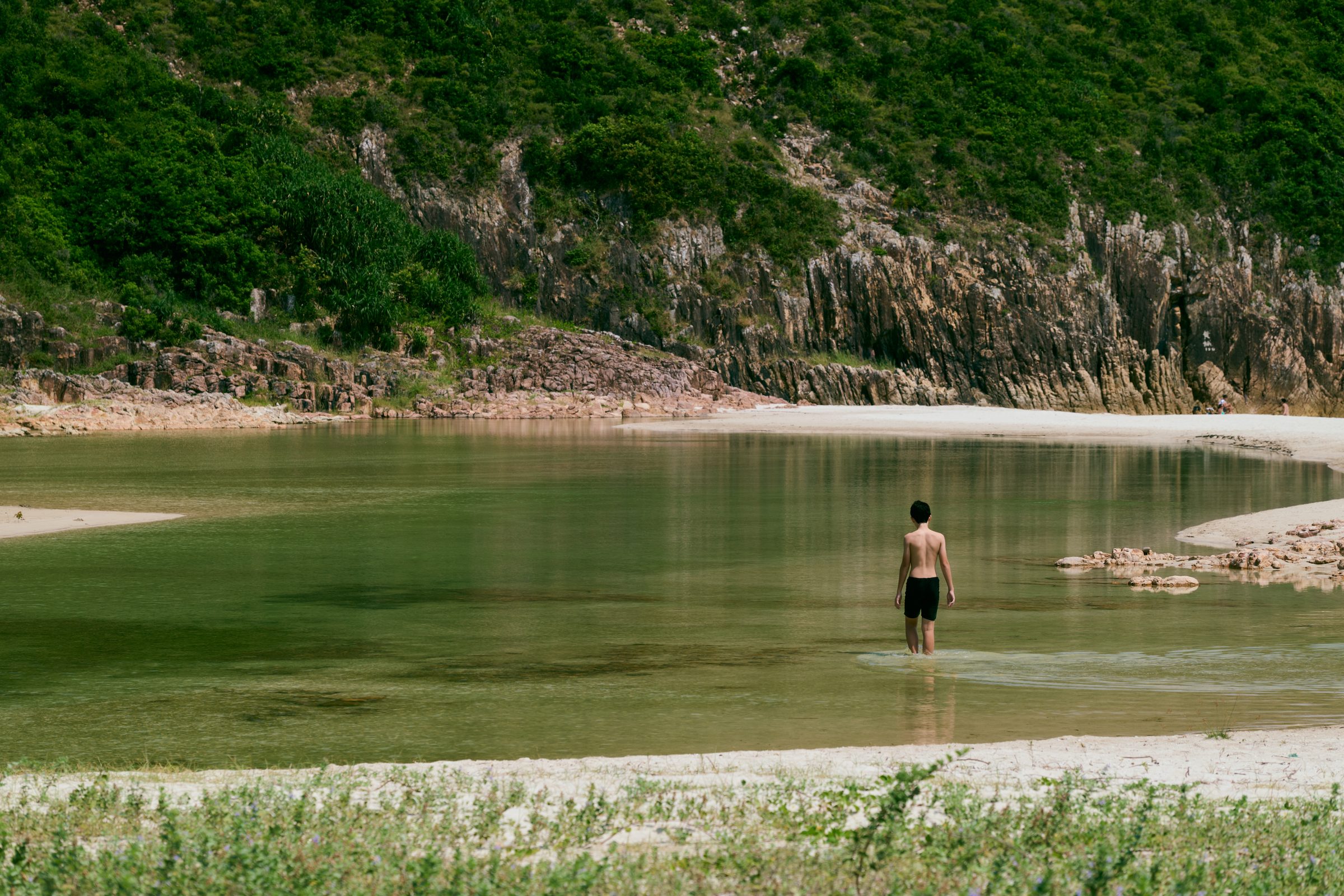 Man wading in a shallow lagoon beneath rock cliffs, MacLehose Trail, Sai Kung, Hong Kong