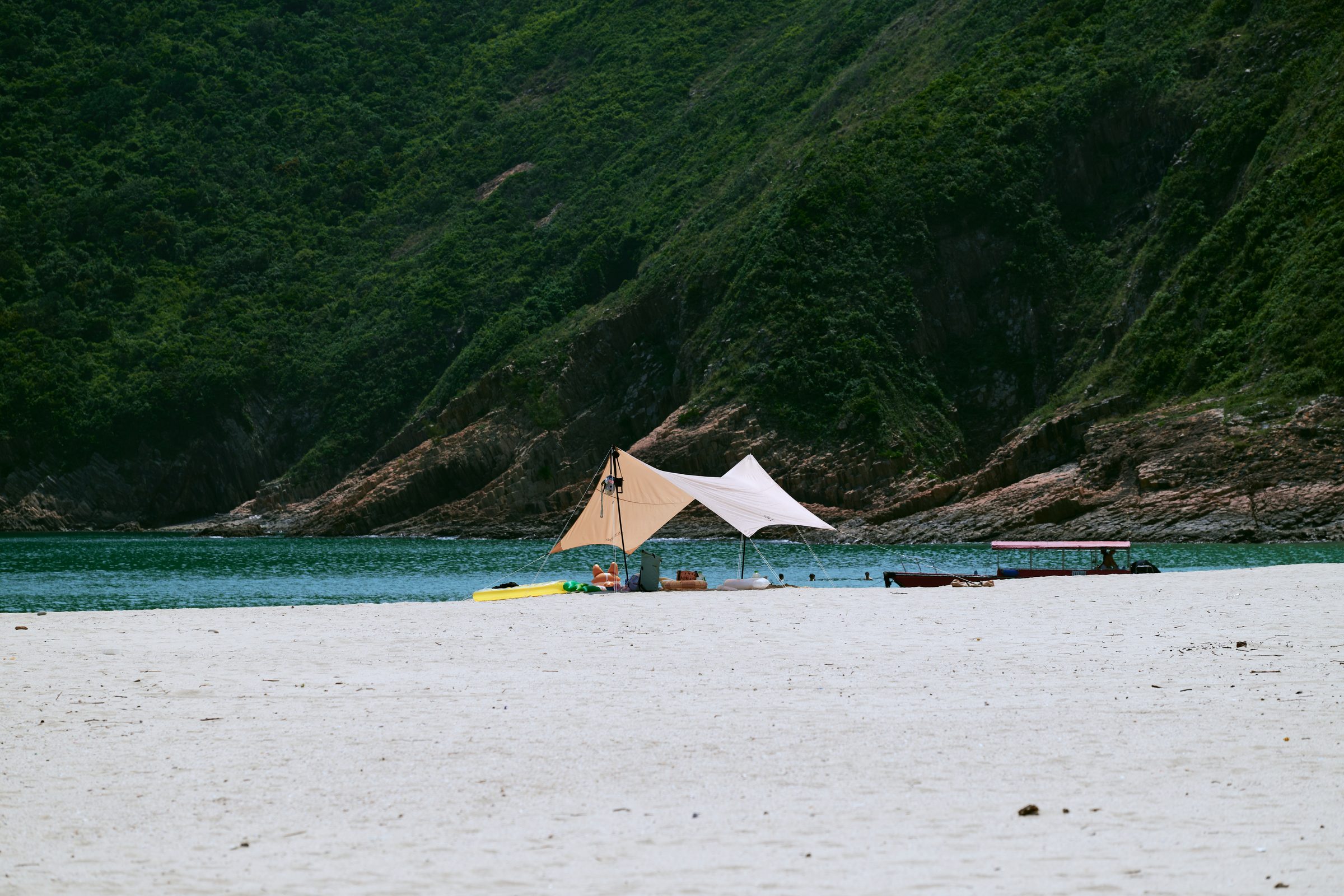 Beach tent on white sand with boats and green hills behind, MacLehose Trail, Sai Kung, Hong Kong