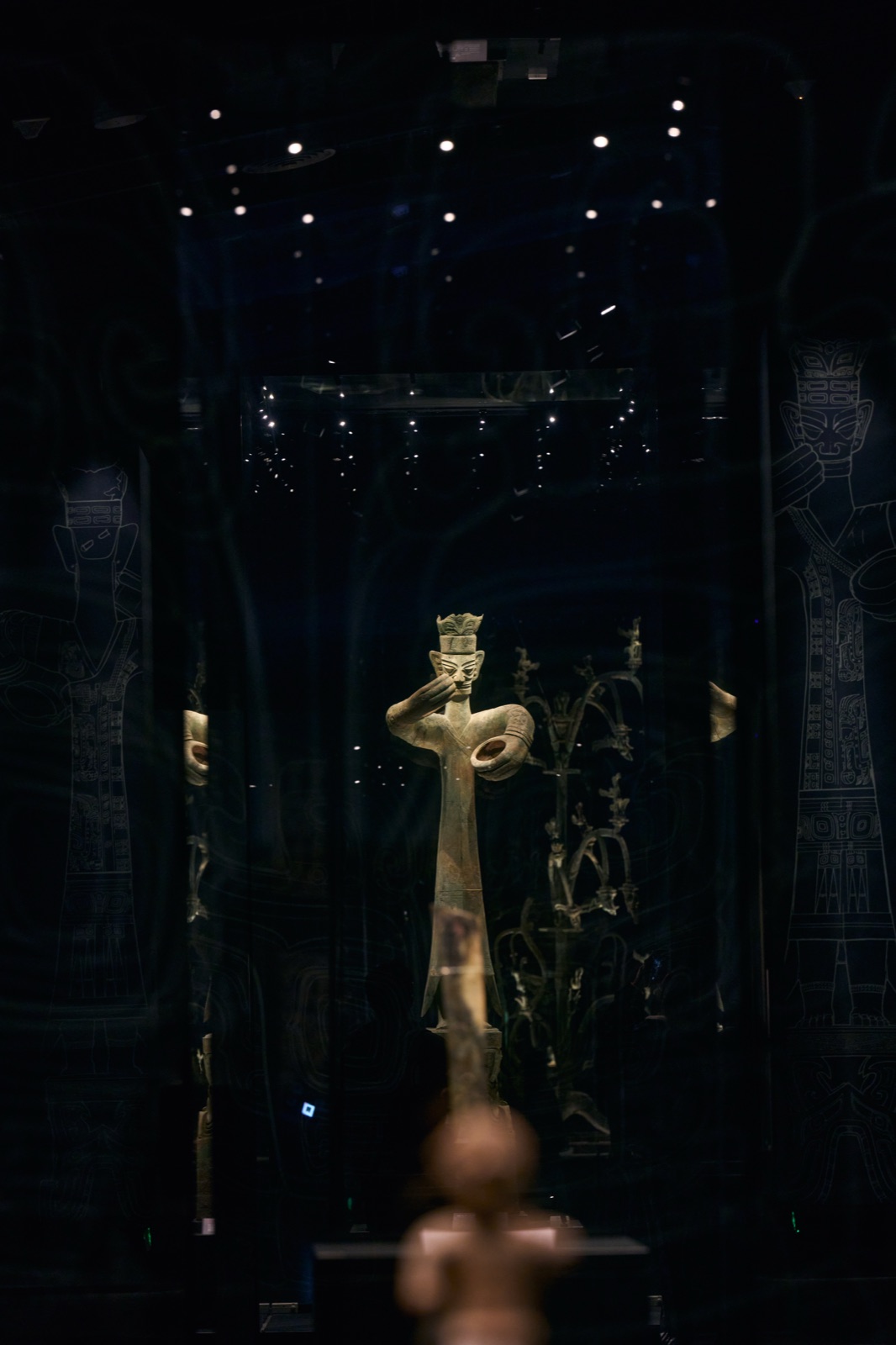 Bronze standing figure seen through glass, with reflected line drawings and star-like lights, Sanxingdui Museum, Guanghan, China
