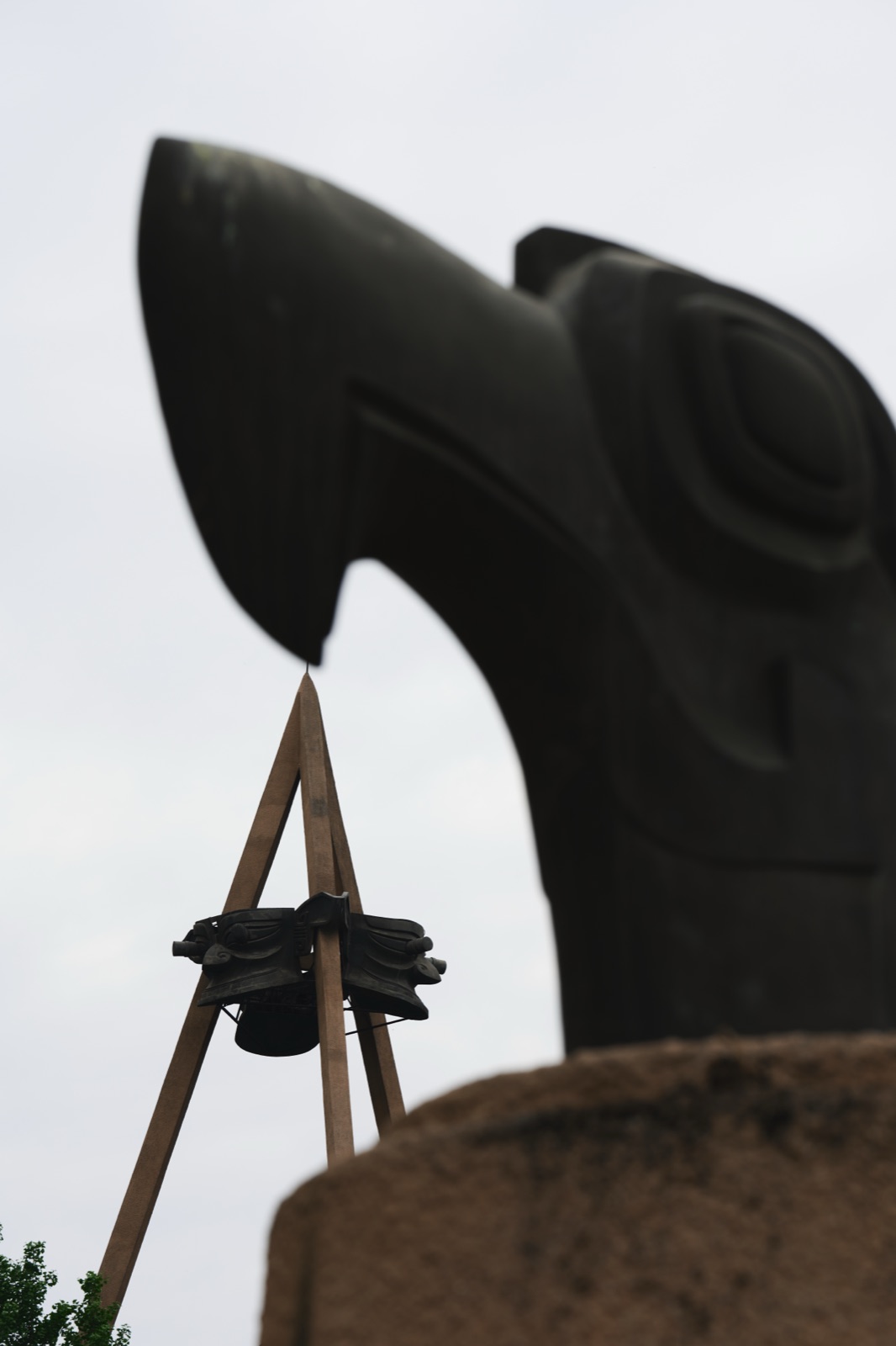 Bird-head sculpture in silhouette outdoors against a grey sky, with a hanging bronze-like structure, Sanxingdui, Guanghan, China